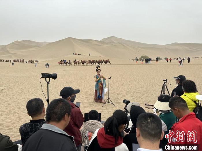 圖為2023年4月底，敦煌大漠“逐舞者”奧楠在鳴沙山月牙泉景區(qū)視頻直播，吸引游人圍觀?！●T志軍 攝